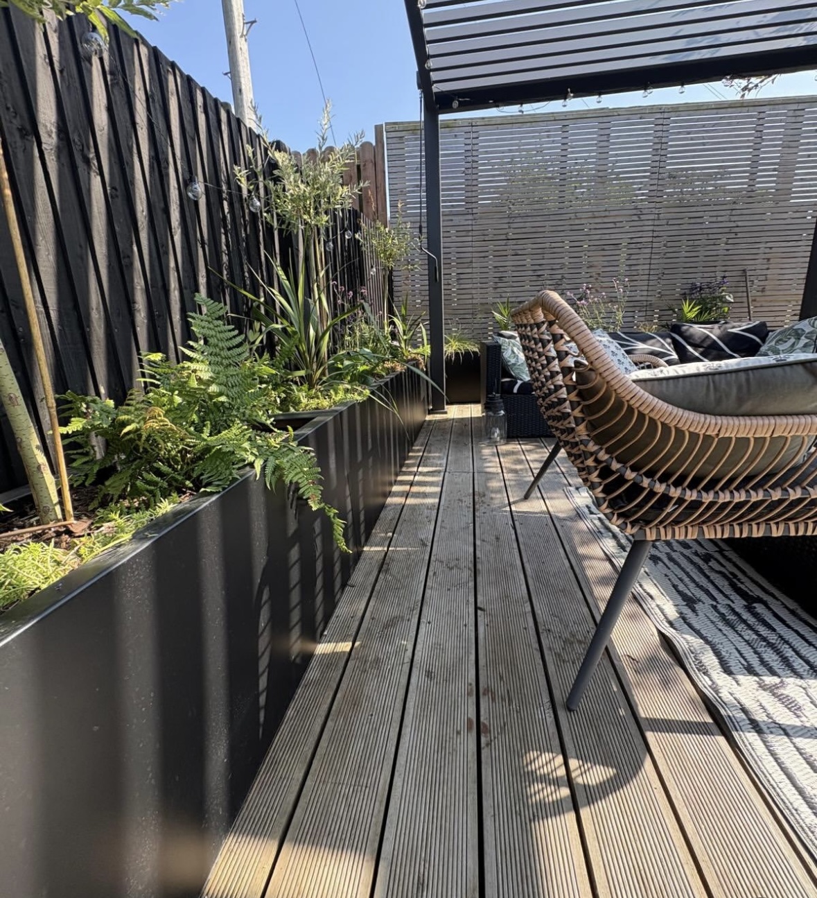Long black powder-coated steel trough planters lining a decked terrace
