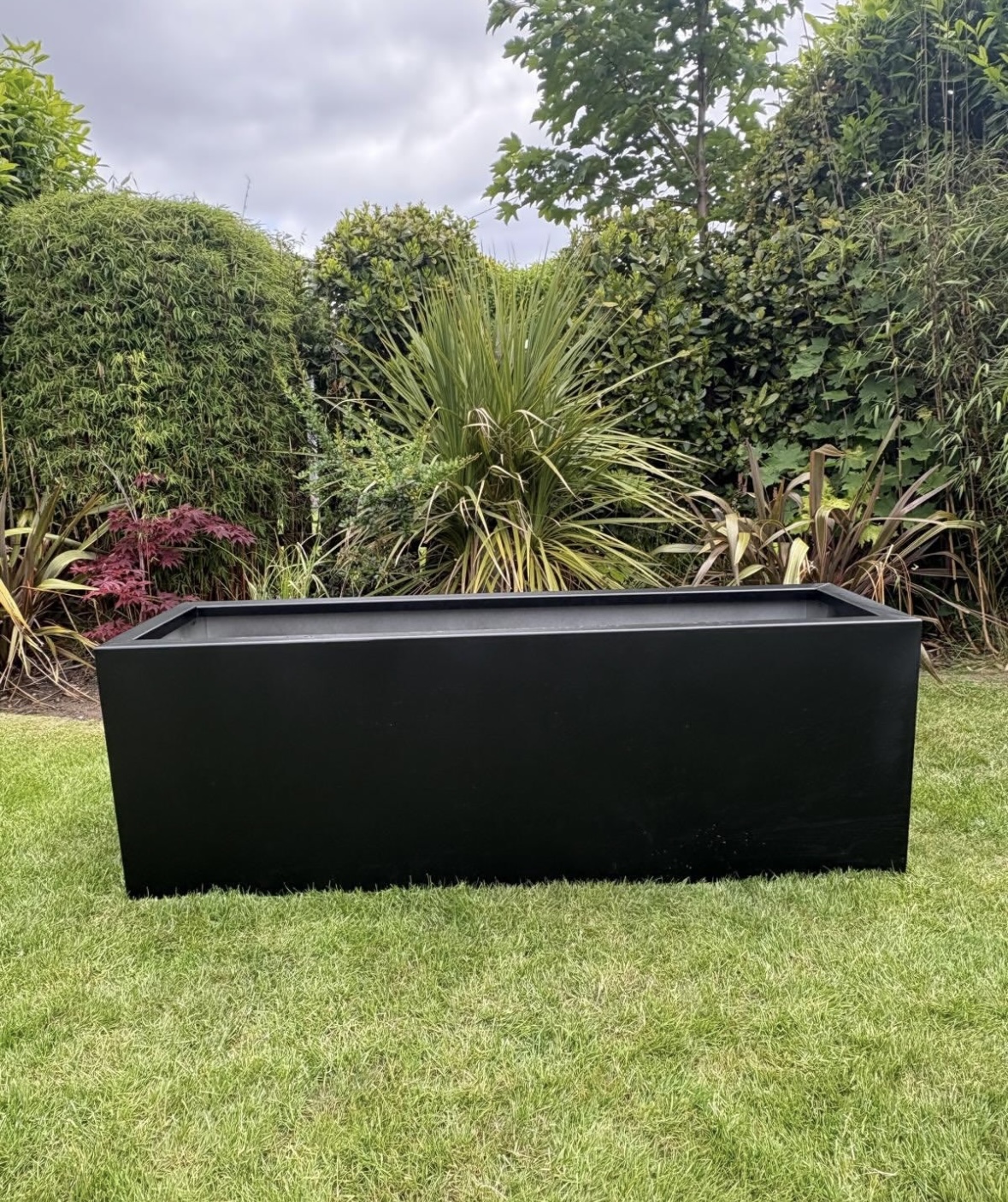 Large rectangular black powder-coated steel planter on a garden lawn